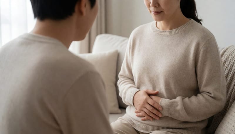 소파에 앉아 손으로 배 상태를 가늠해보는 여성