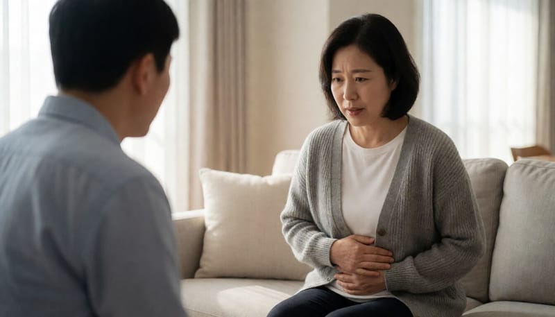 소파에 앉아 배를 만지며 표정을 찌푸린 여성