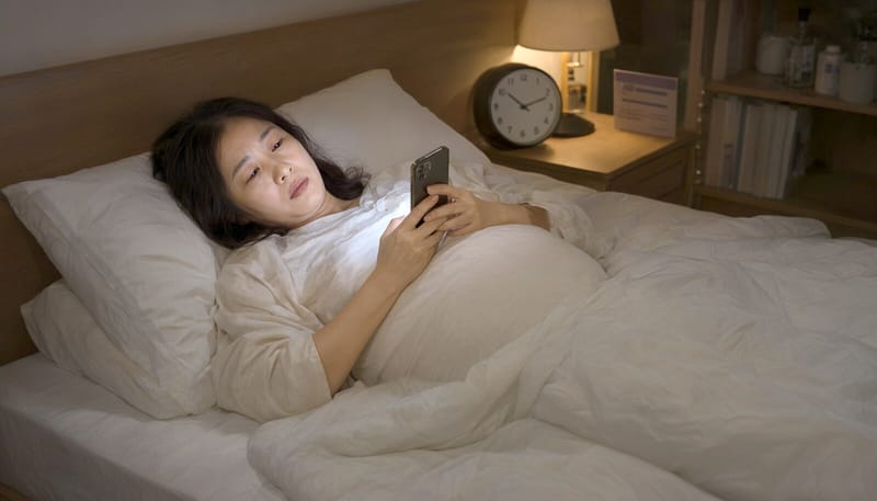 임신부가 어두운 방에서 늦은 밤까지 스마트폰을 보는 모습
